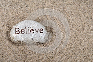 Word believe on stone in sand