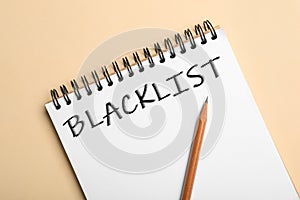 Word Blacklist written in notepad on beige background, top view