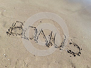 Word `Bonus` written on wet sand at the sea