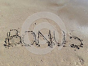 Word `Bonus` written on wet sand at the sea