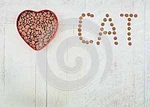 Word cat and food for pets in the heart shaped bowl on wooden background. With love for cats concept. Top view. Copy