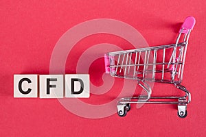 The word CFD - Contract For Difference, on wooden cubes, on a pink background with a shopping trolley