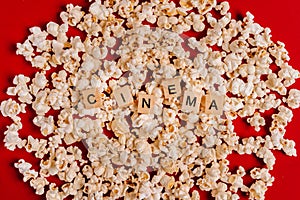The word `CINEMA` made of wooden blocks lies on popcorn on a red background. The concept of recreation with watching movies