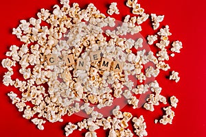 The word `CINEMA` made of wooden blocks lies on popcorn on a red background. The concept of recreation with watching movies