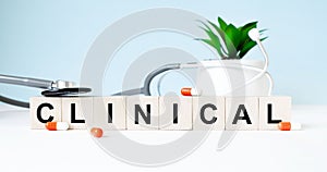 The word CLINICAL is written on wooden cubes near a stethoscope on a wooden background. Medical concept