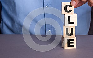 The word CLUE the man composes from wooden cubes vertically photo