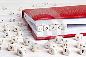 Word Coach written in wooden blocks in red notebook on white woo