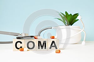 The word COMA is written on wooden cubes near a stethoscope on a wooden background. Medical concept