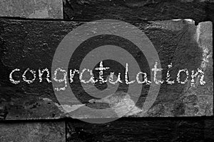 The word congratulation written with chalk on black stone.
