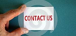 Word `contact us` on the white card between fingers. Beautiful blue background, business concept. Copy space