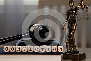 Word CONVICTION composed of wooden dices. Wooden gavel and statue of Themis in the background