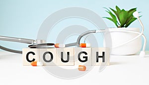 The word COUGH is written on wooden cubes near a stethoscope on a wooden background. Medical concept