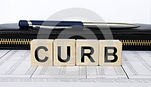 A word Curb written in a wooden cube with a pen and wallet