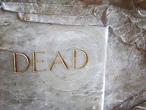 The word dead carved into marble on a sarcophagus casket inside a church