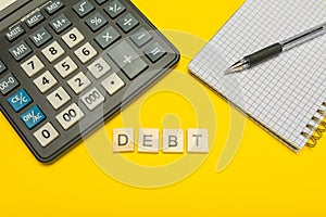 Word debt made with wood letters on yellow background and modern calculator with pen and notebook. Copy space. Economy, money