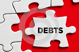 The word debts on a puzzle piece with red background. Financial debt