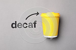 Word Decaf and arrow pointing at takeaway paper coffee cup on light grey background, top view