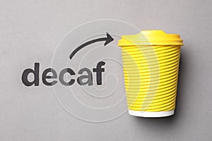 Word Decaf and arrow pointing at takeaway paper coffee cup on light grey background, top view