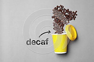 Word Decaf and arrow pointing at takeaway paper cup with coffee beans on light grey background, flat lay. Space for text