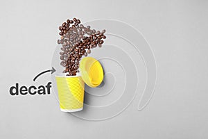 Word Decaf and arrow pointing at takeaway paper cup with coffee beans on light grey background, flat lay. Space for text