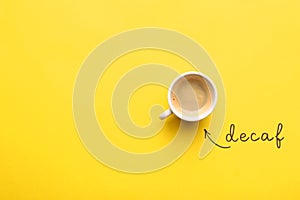 Word Decaf and cup of coffee on yellow background, top view. Space for text