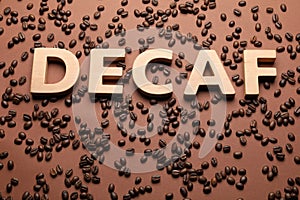 Word Decaf made of wooden letters on brown background with coffee beans