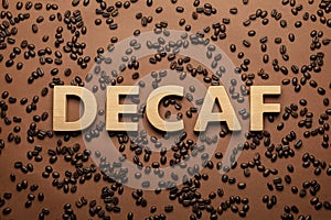 Word Decaf made of wooden letters on brown background with coffee beans, flat lay