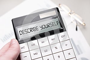 The word DESCRIBE YOURSELF is written on the calculator. Business man holding a calculator in his hand