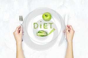 Word DIET arranged of garden peas on a large white plate, a fresh green apple and a soft tape measure on a concrete table.