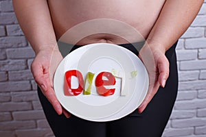 Word diet carved of vegetables on the plate in hands of overweig