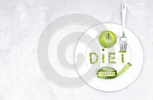 Word DIET made of garden peas on a large white plate with a fresh green apple, a soft tape measure and a fork on a concrete table