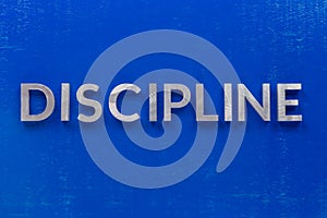 The word discipline laid with silver metal characters on blue painted wooden board in central flat lay composition