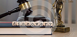 Word DISCOVERY composed of wooden dices. Wooden gavel and statue of Themis in the background photo