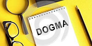 Word dogma printed on white notepad on office table