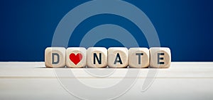 The word donate on wooden blocks with heart icon against blue background. Charity and donation