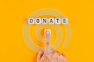 The word donate written on wooden cubes with a male hand pushing the button for donation. Charity concept