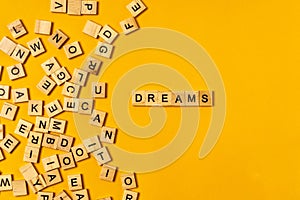 The word `DREAMS` is made of wooden letters on a bright yellow background next to a bunch of other letters. Motivational Words Qu