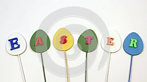 Word Easter isolated on white background, minimalism. Inscription Easter on multicolored egg sticks.