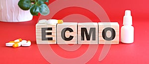The word ECMO is made of wooden cubes on a red background. Medical concept