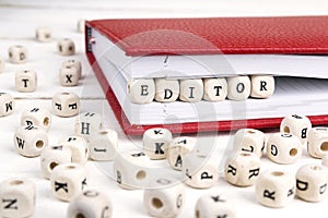 Word Editor written in wooden blocks in red notebook on white wooden table.