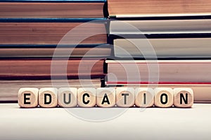 The word education on wooden cubes with stacked books background. Education, school and learning concept