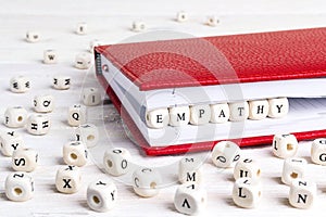 Word Empathy written in wooden blocks in red notebook on white w