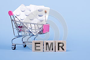 The word EMR - electronic medical record, on wooden cubes, on a blue background with pills in a shopping trolley