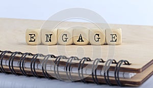Word ENGAGE made with letters on wooden blocks on wooden notepad