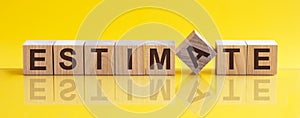 Word ESTIMATE is made of wooden building blocks lying on the table and on a light yellow background. Concept