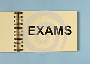 Word EXAMS on paper of notebook on blue background