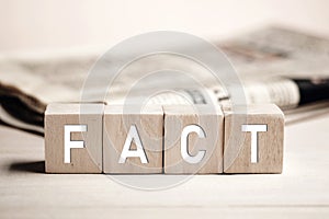 The word fact on wooden blocks against a newspaper background. Reliable, honest and accurate news making in media concept