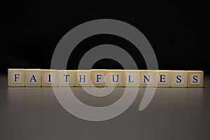 The word FAITHFULNESS written on wooden cubes isolated on a black background
