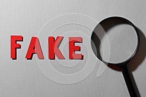 Word Fake made of red letters and magnifying glass on grey background, flat lay