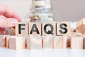 The word Faqs on the wooden blocks and a bank with money in the background